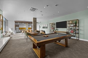 A pool table is in the middle of a room with a TV on the wall.